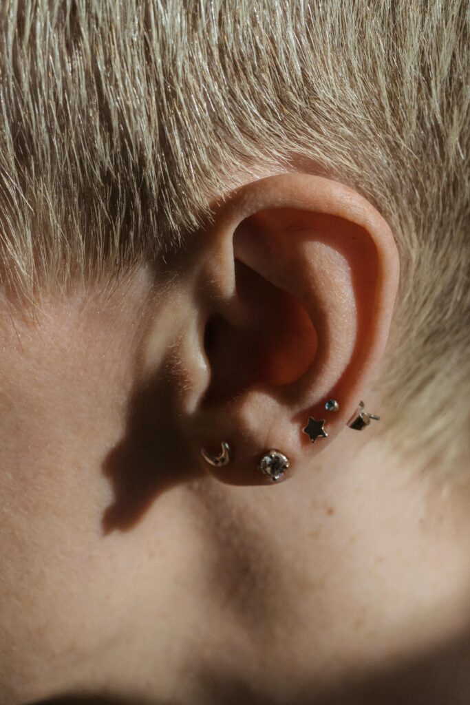 Detailed shot of a woman's pierced ear adorned with various earrings in a sunlit setting.
