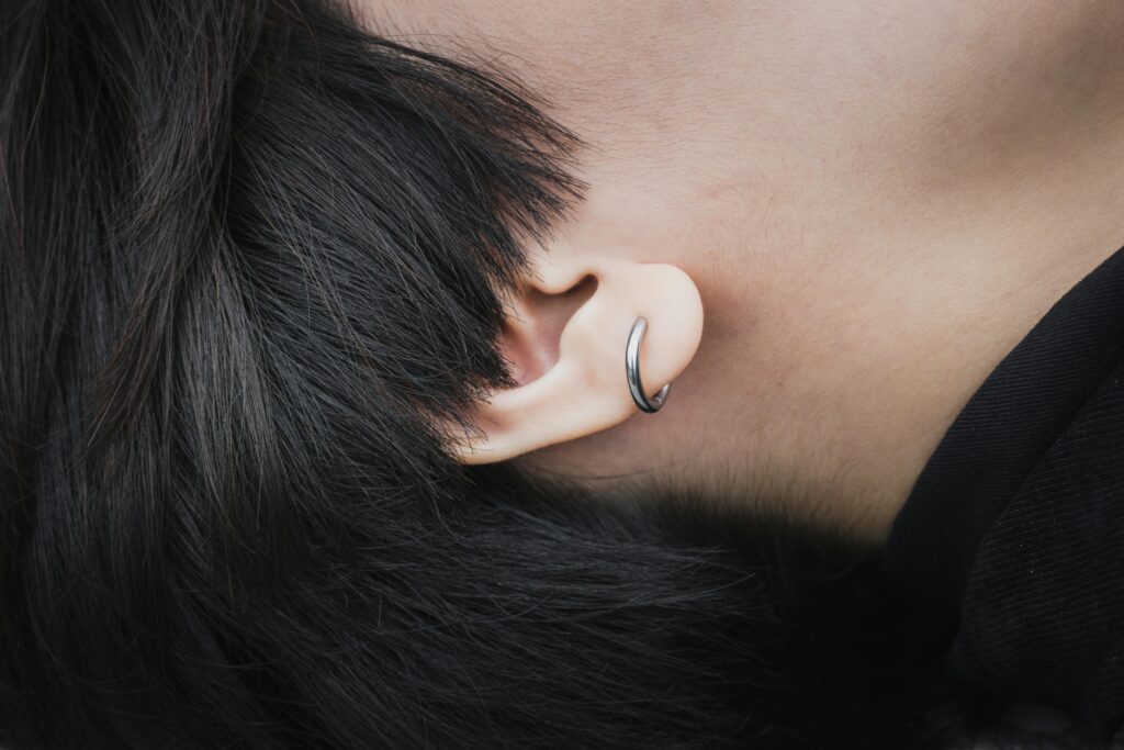 Detailed close-up of an ear featuring a silver hoop earring and black hair.